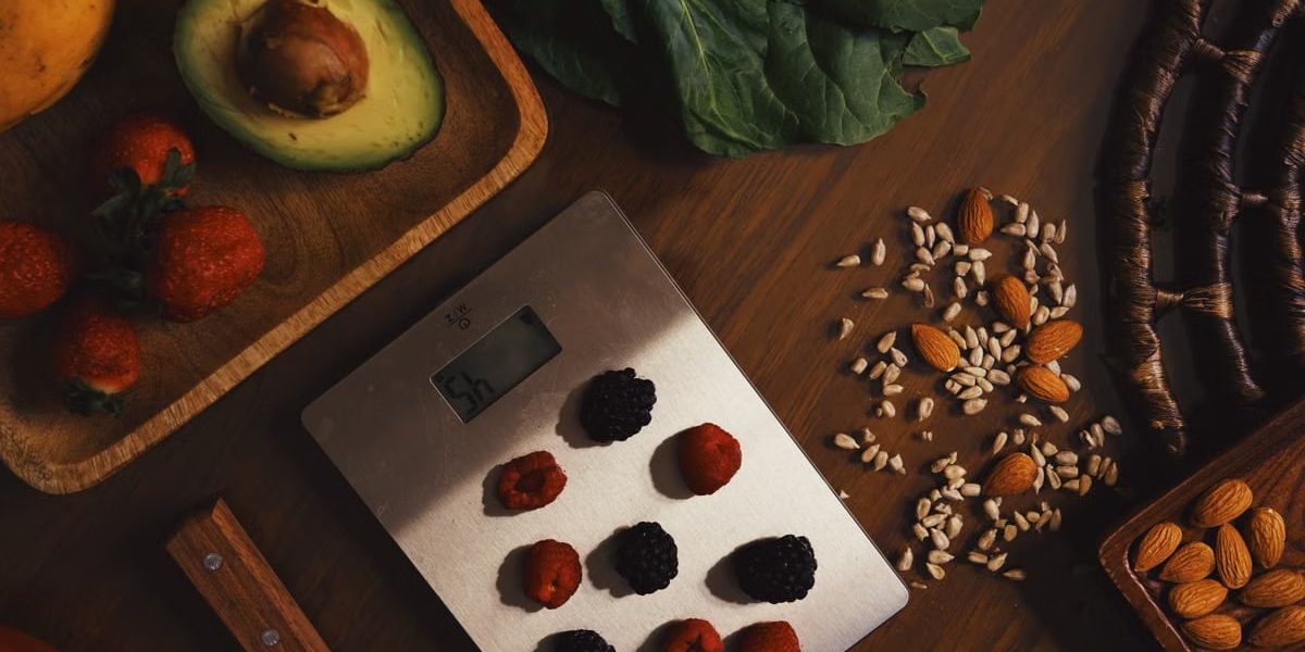 Top view of composed raw almond with seeds and avocado on table with berries on scales for cooking healthy dish